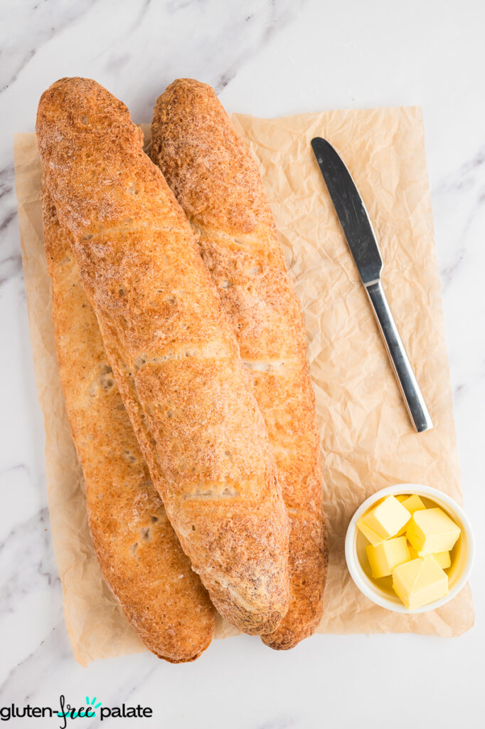 Baguettes on baking paper with butter and a knife.