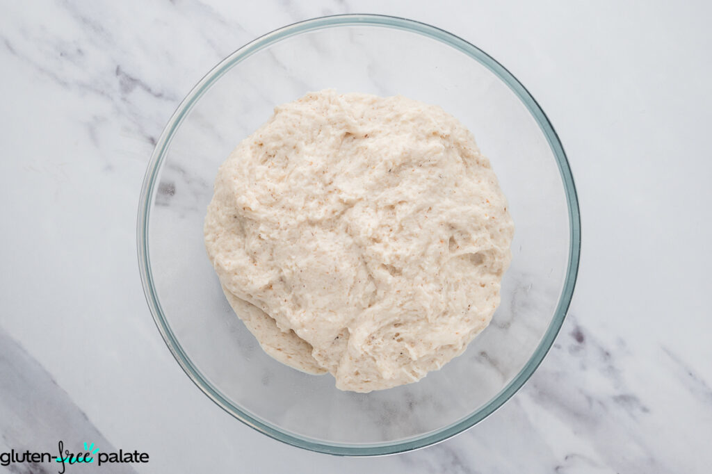 Gluten-free baguette dough mixed together in a glass bowl, sticky and elastic in texture.