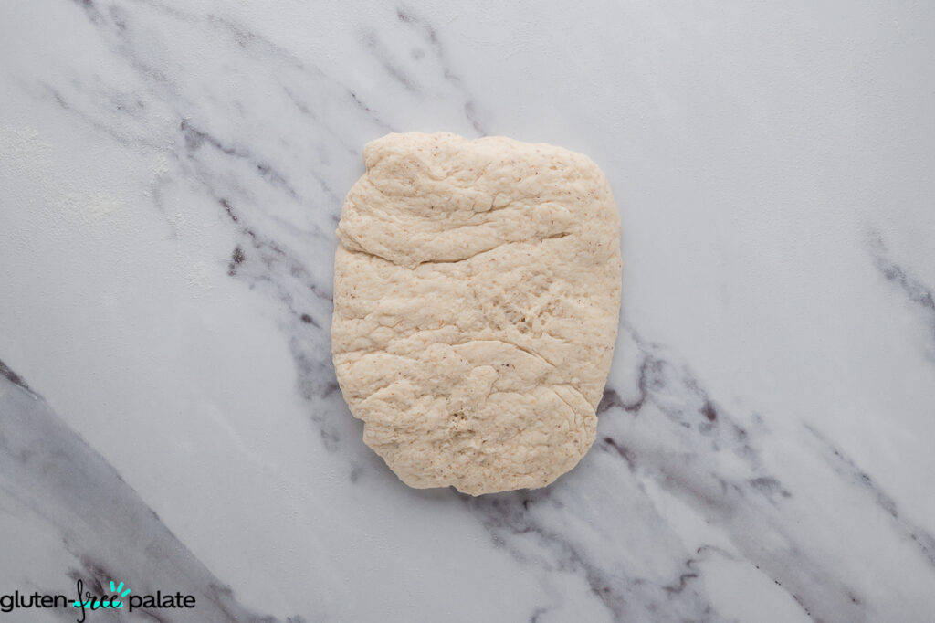 A piece of gluten-free dough placed on a lightly floured marble surface in a rectangle format.