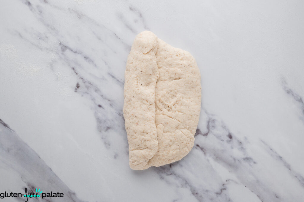 Gluten-free dough folded lengthwise over itself on the work surface.