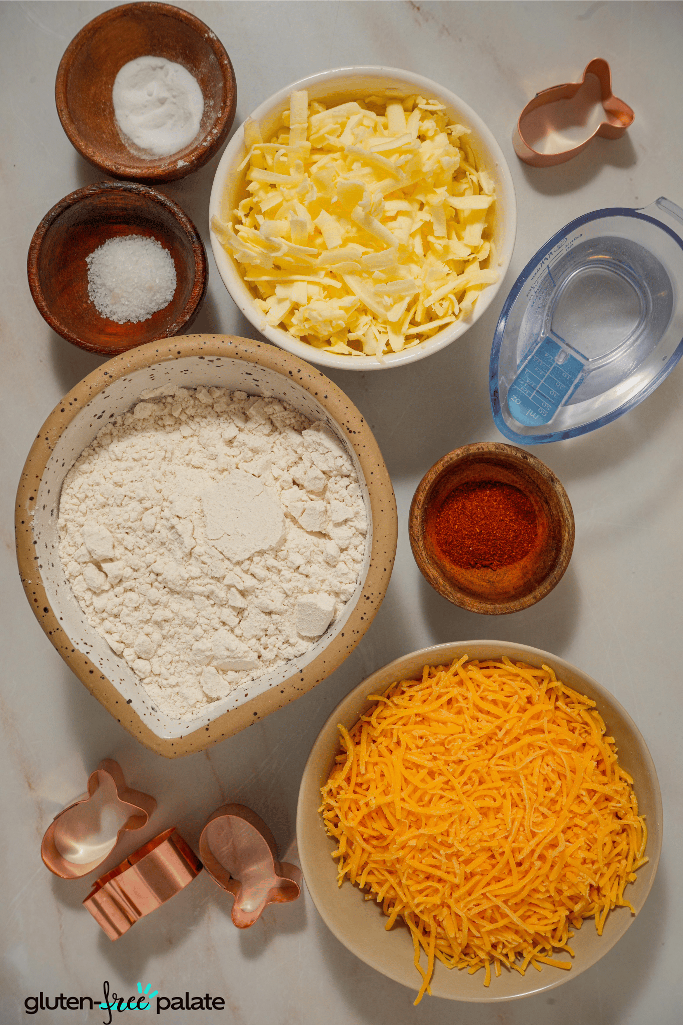 Ingredients for gluten-free goldfish crackers laid out on a surface: gluten-free flour, sharp cheddar cheese, butter, and seasonings