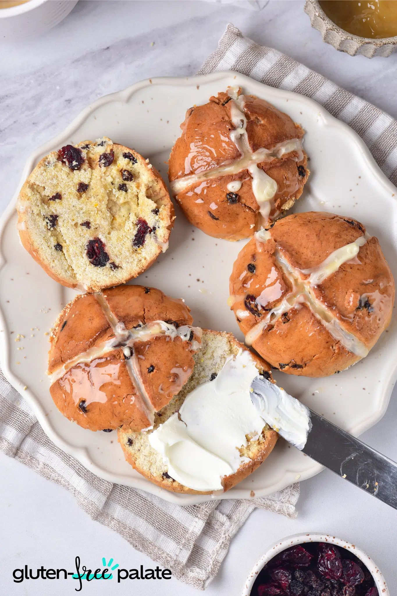 gluten-free hot cross buns on a white plate. Once is sliced with butter on it.