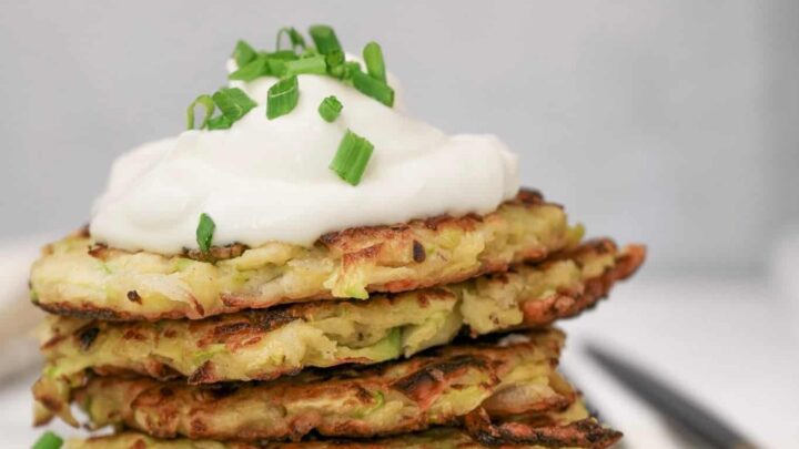 Gluten-free zucchini fritters stacked on a plate topped with dip.