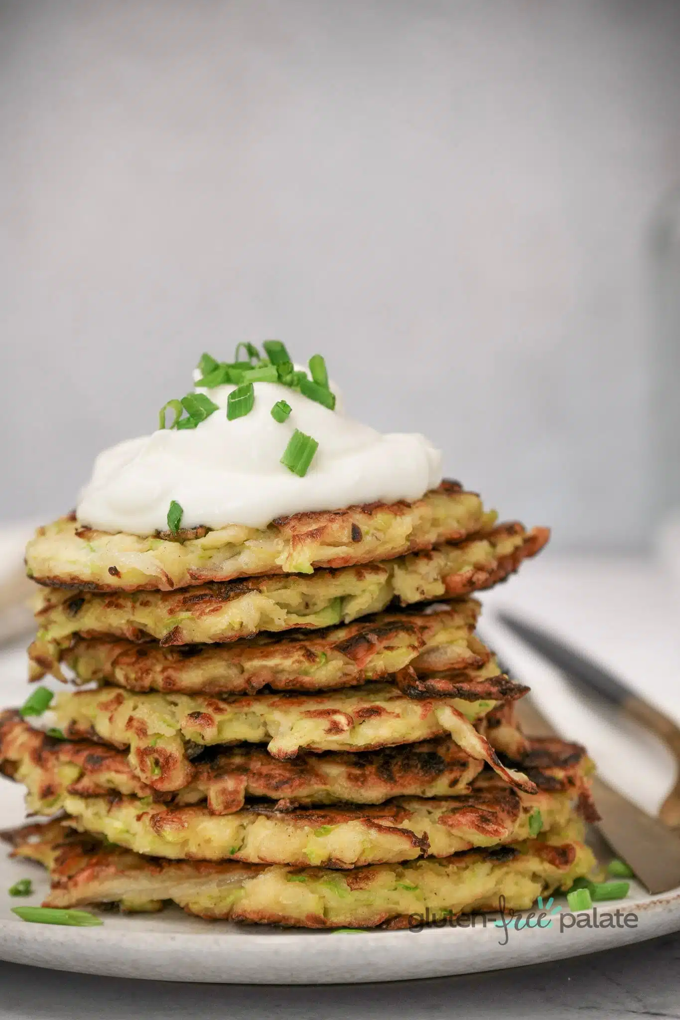Gluten-free zucchini fritters stacked on a plate topped with dip.