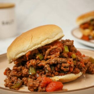 Close up view of a gluten-free sloppy joes on a white plate showing the filling in a gluten-free bun