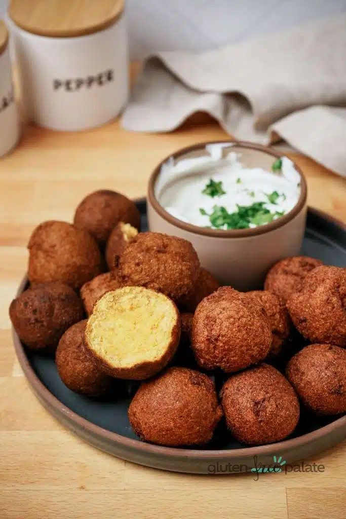 Gluten-free hush puppies showing the inside of one and a plate filled with them.