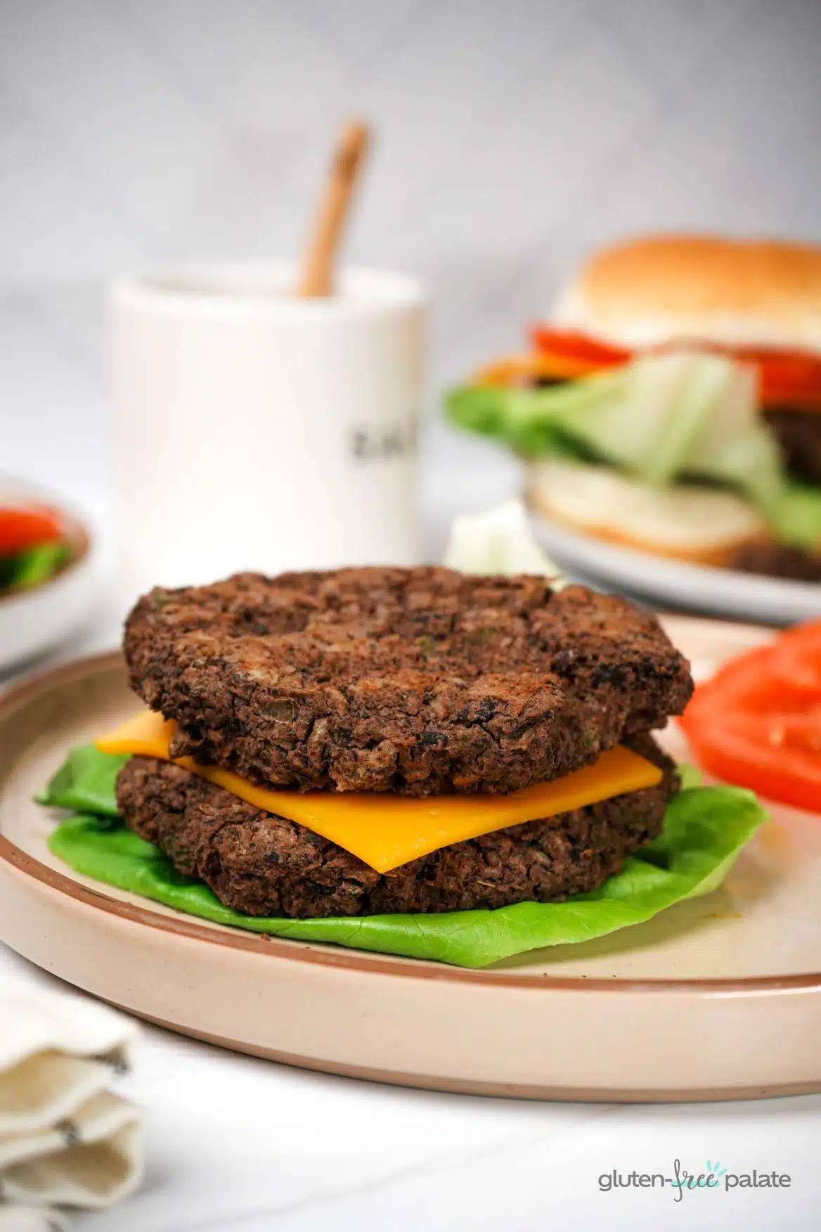 Gluten-free black bean burgers patties on top of each other with lettuce on the bottom and cheese in the middle.