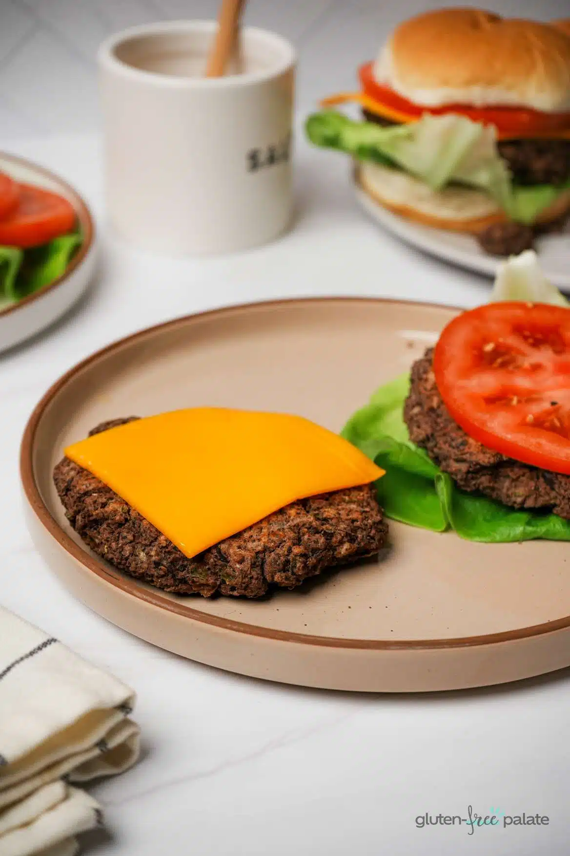 Gluten-free black bean burgers on a brown plate with cheese, lettuce, and tomato.