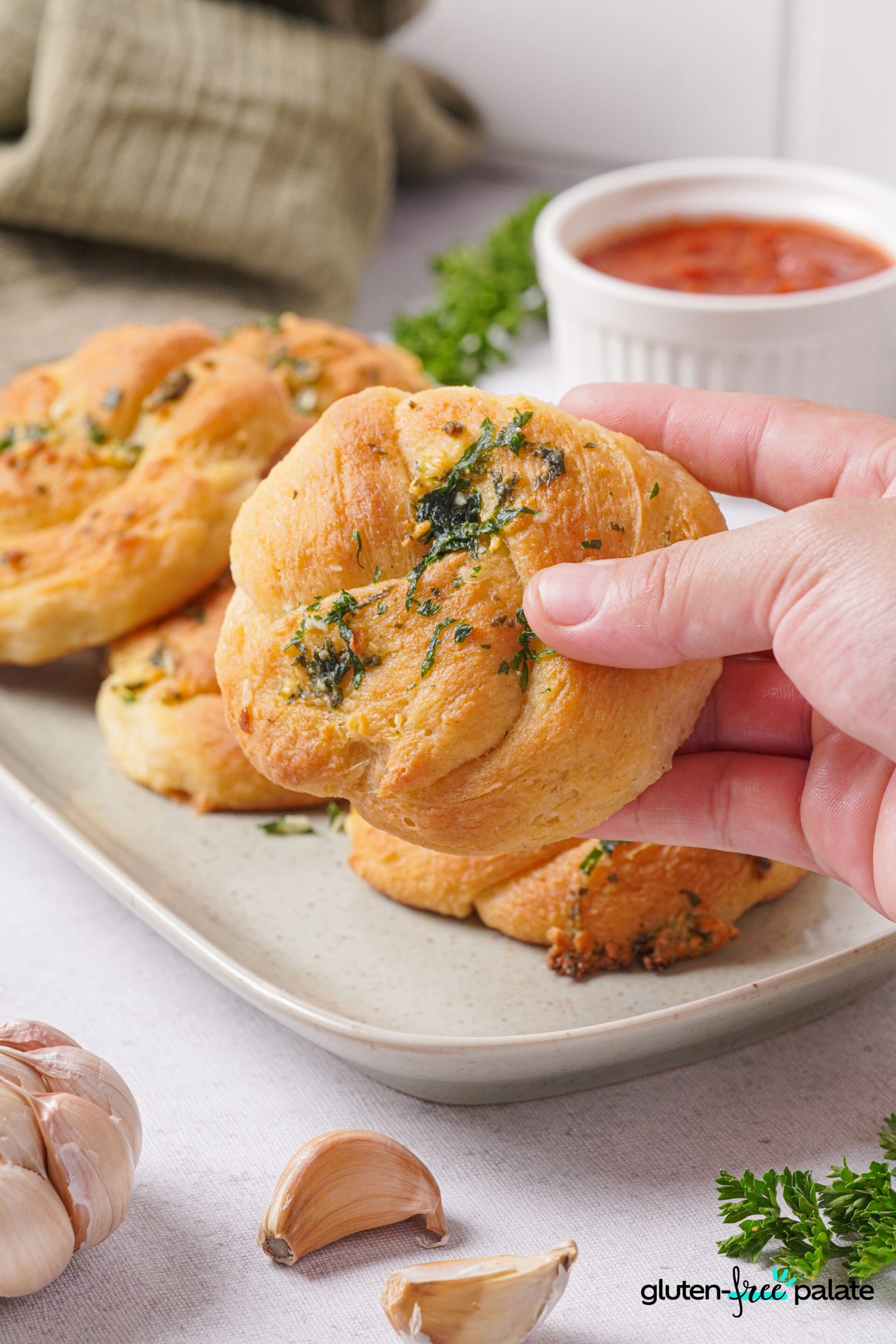 Gluten-free garlic knots on a white plate with toppings and one being held in a hand.