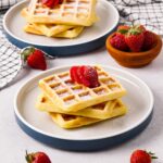 Gluten-free Belgian waffles on a plate topped with strawberries.