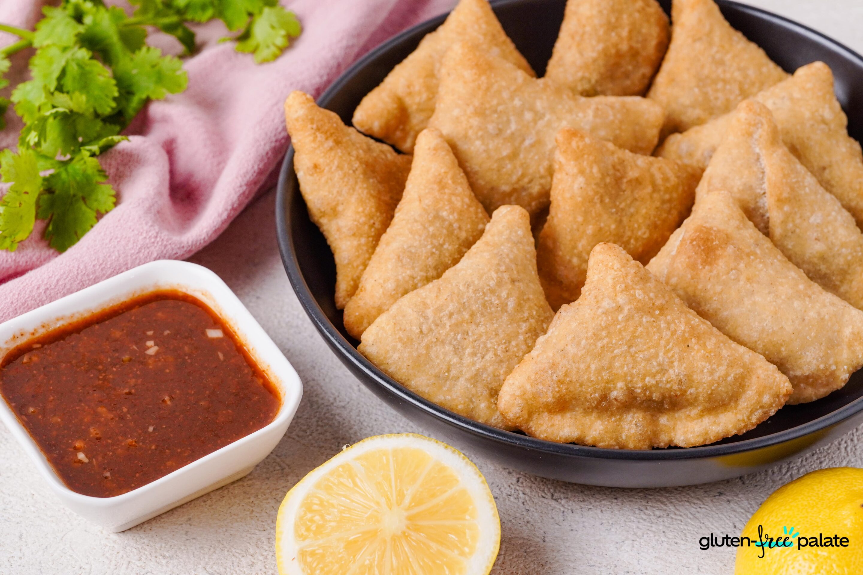 Gluten-free samosas in a black plate with sauce.