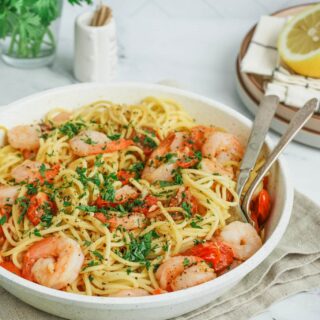 Gluten-Free Shrimp Scampi in a beige bowl on a counter with serving spoons.