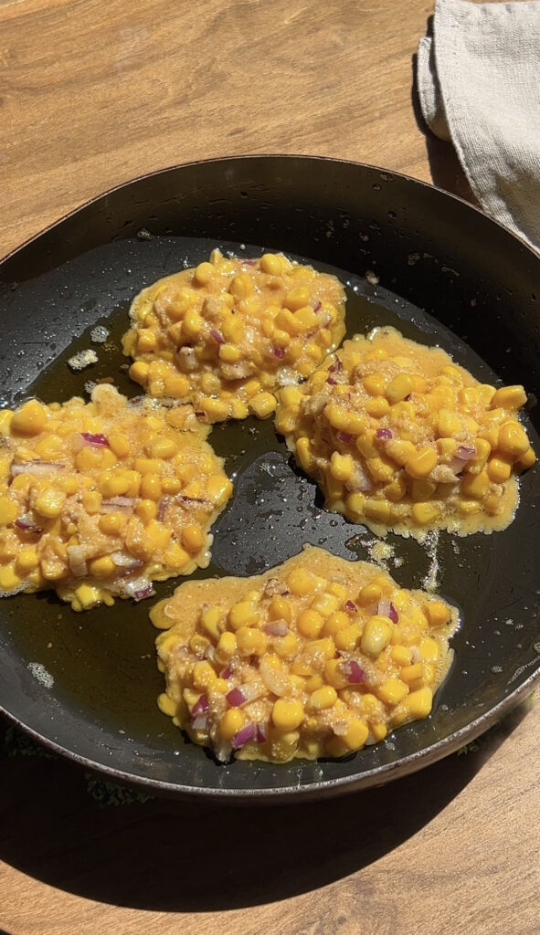 Corn fritters in a frying pan being cooked.