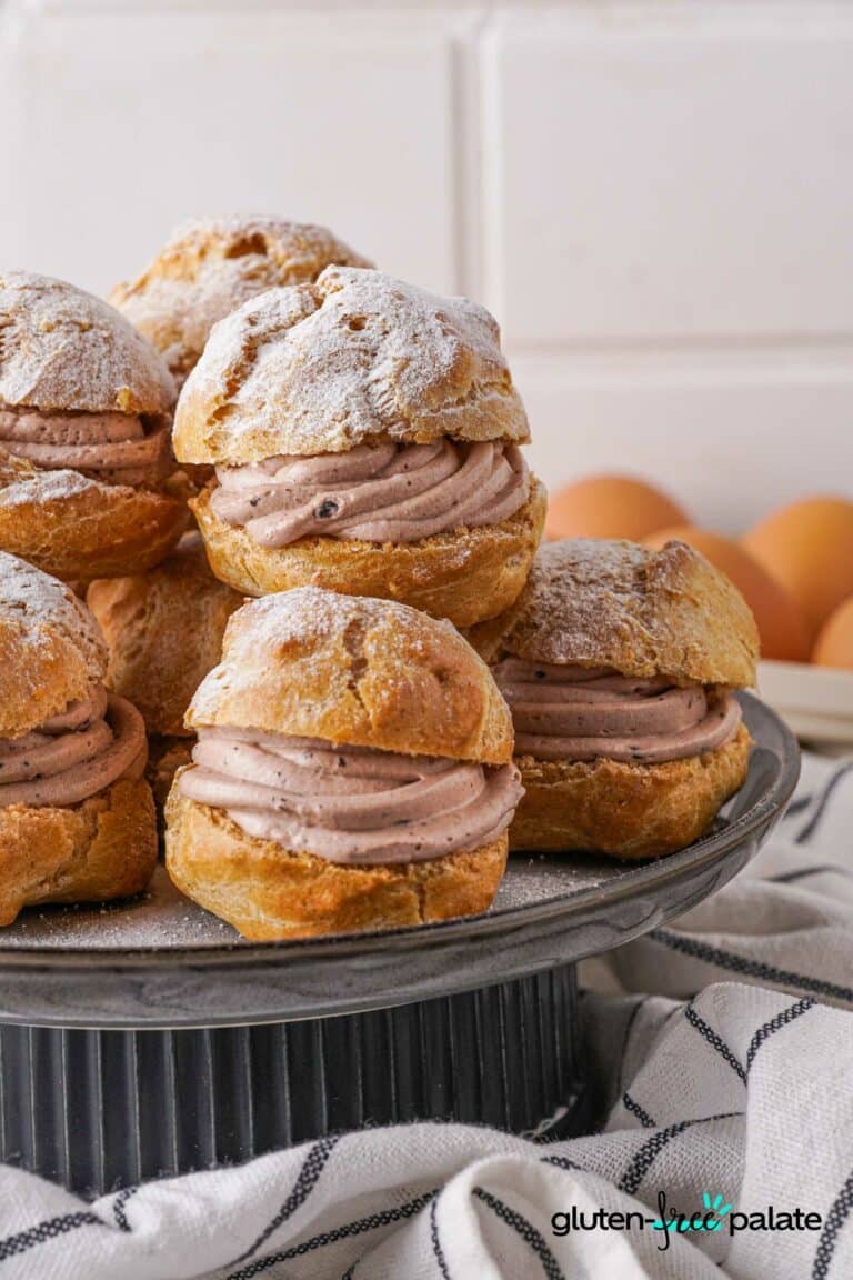Gluten-Free Choux Pastry made into cream puffs on a cake stand with icing sugar on top.