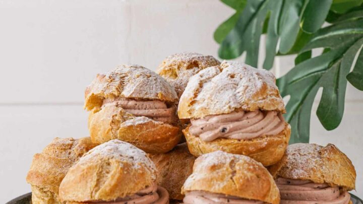 Gluten-Free Choux Pastry made into cream puffs on a cake stand with icing sugar on top.
