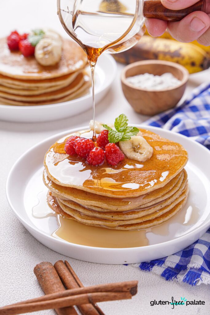 Gluten-Free Banana Pancakes stacked on a white plate with berries, bananas and mint.