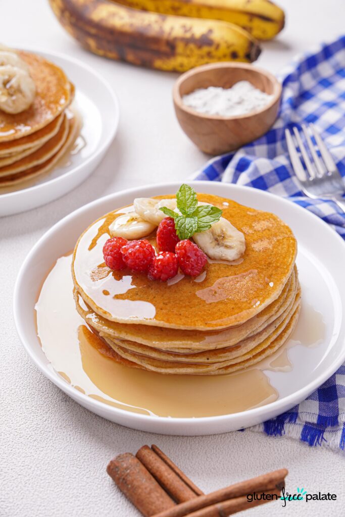 Gluten-Free Banana Pancakes stacked on a white plate with berries, bananas and mint.