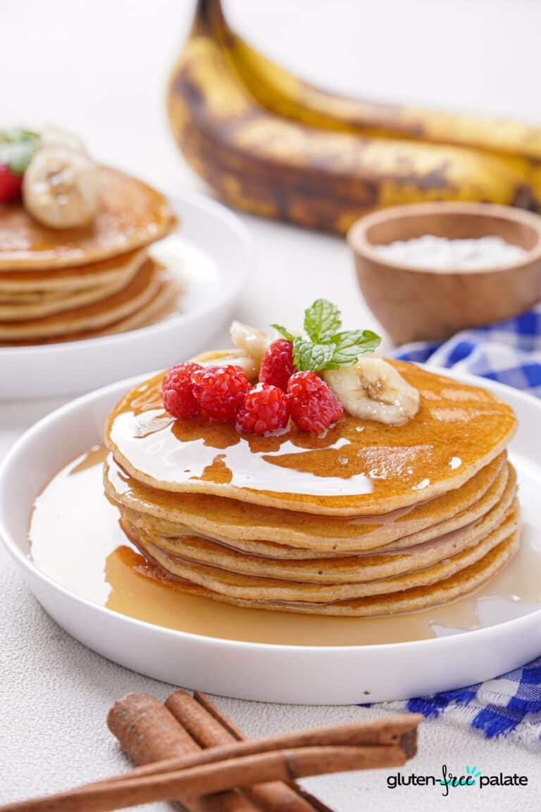 Gluten-Free Banana Pancakes stacked on a white plate with berries, bananas and mint.