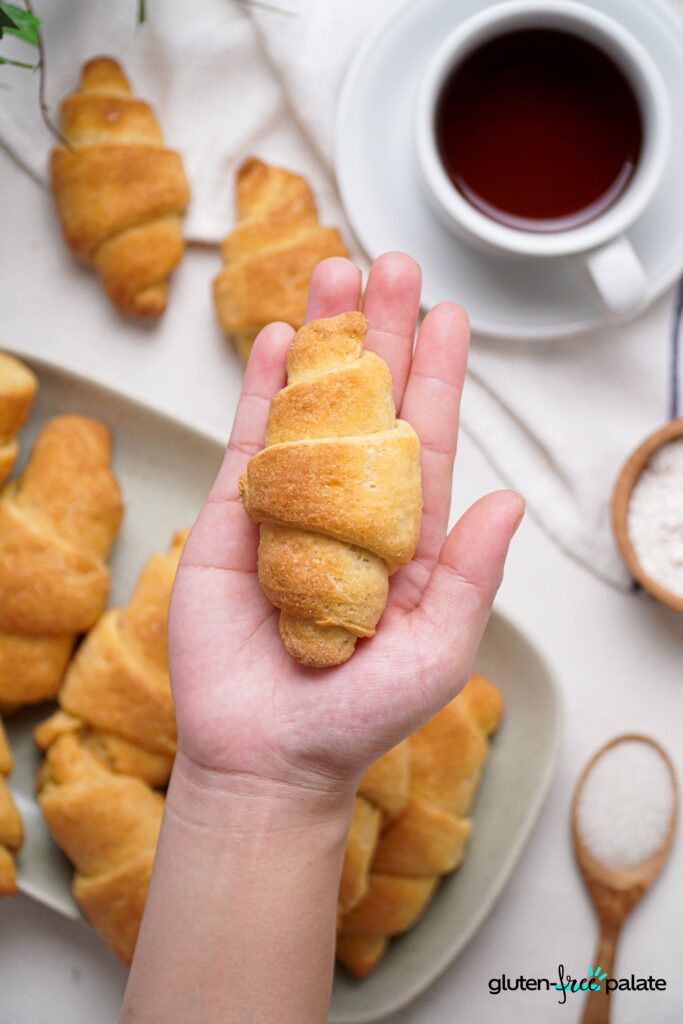 Gluten-Free Crescent rolls held in a hand with a cup of tea in the background. Use these to make breakfast sandwiches.