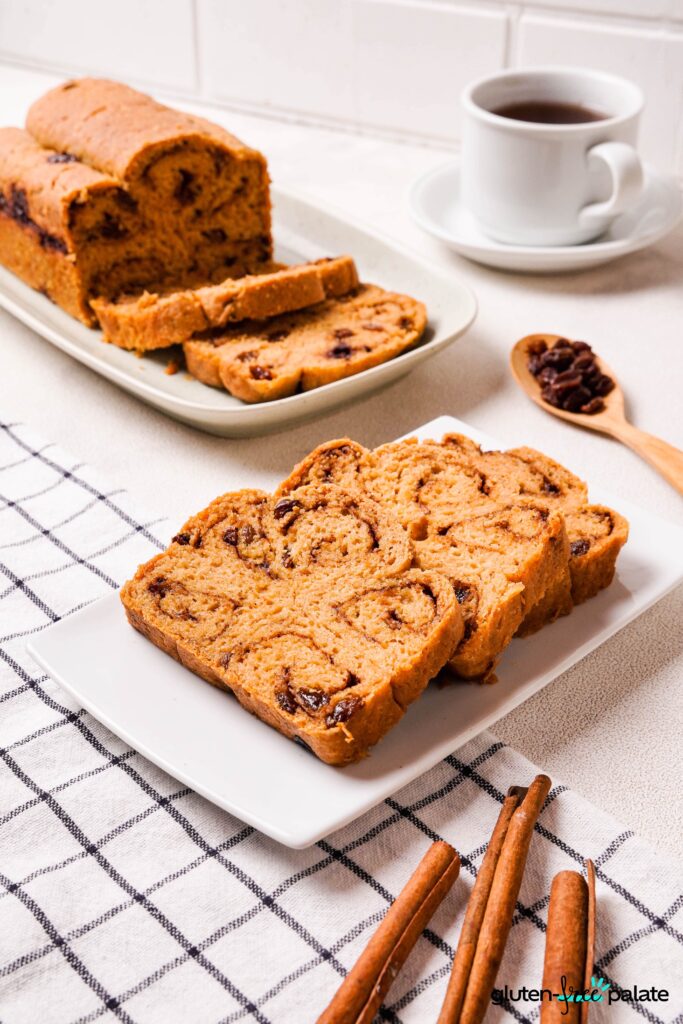 Gluten-Free Cinnamon Raisin Bread on a white plate sliced with coffee and cinnamon sticks.