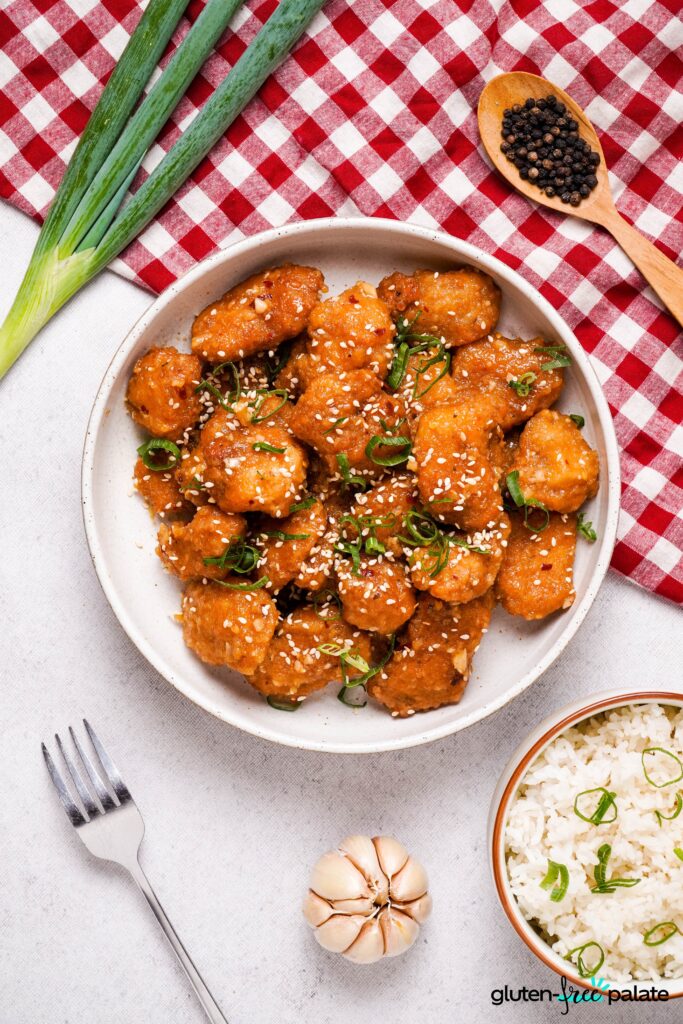 Gluten-Free Sesame Chicken in a brown speckled bowl with ingredients surrounding it.