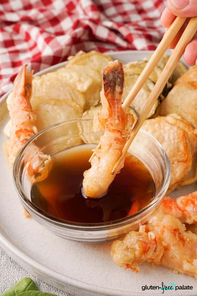 Gluten-free tempura prawn being dipped into the dipping sauce.