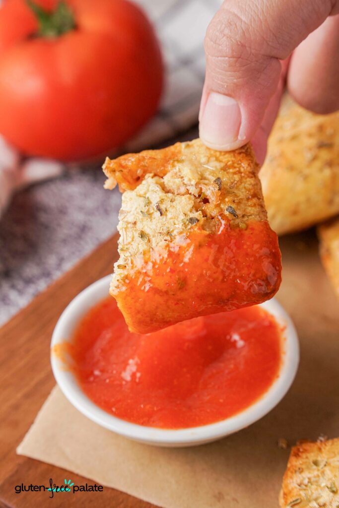 A Gluten-Free Pizza roll being dipped into a sauce.