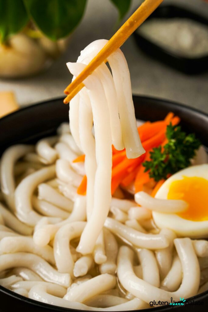 Gluten-Free Udon Noodles being held in chopsticks.