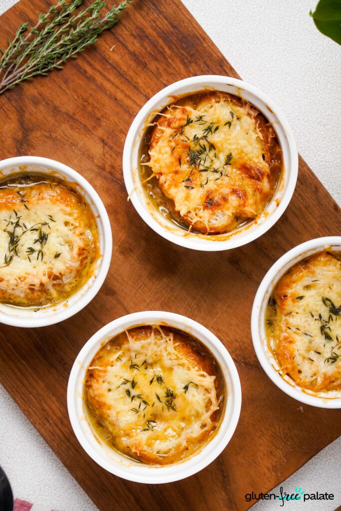 Close up view of Gluten-Free French onion soups in a white ramekins on a wooden board.