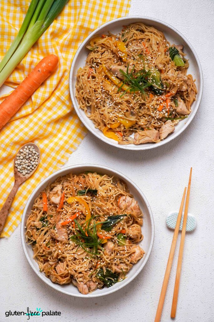 Overhead view of two white plates of Gluten-Free Lo Mein with garnishes.