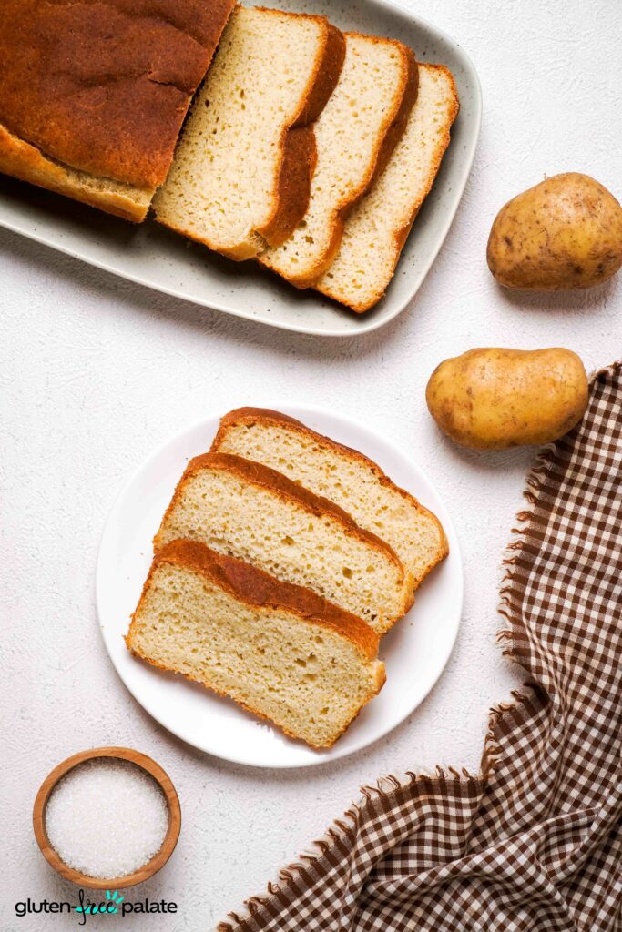 Several slices of gluten-free potato bread stacked on a wooden board, showing a soft, moist crumb ideal for sandwiches.