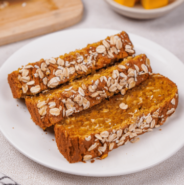 Three slices of gluten free pumpkin bread on a white plate with fresh pumpkin in the background