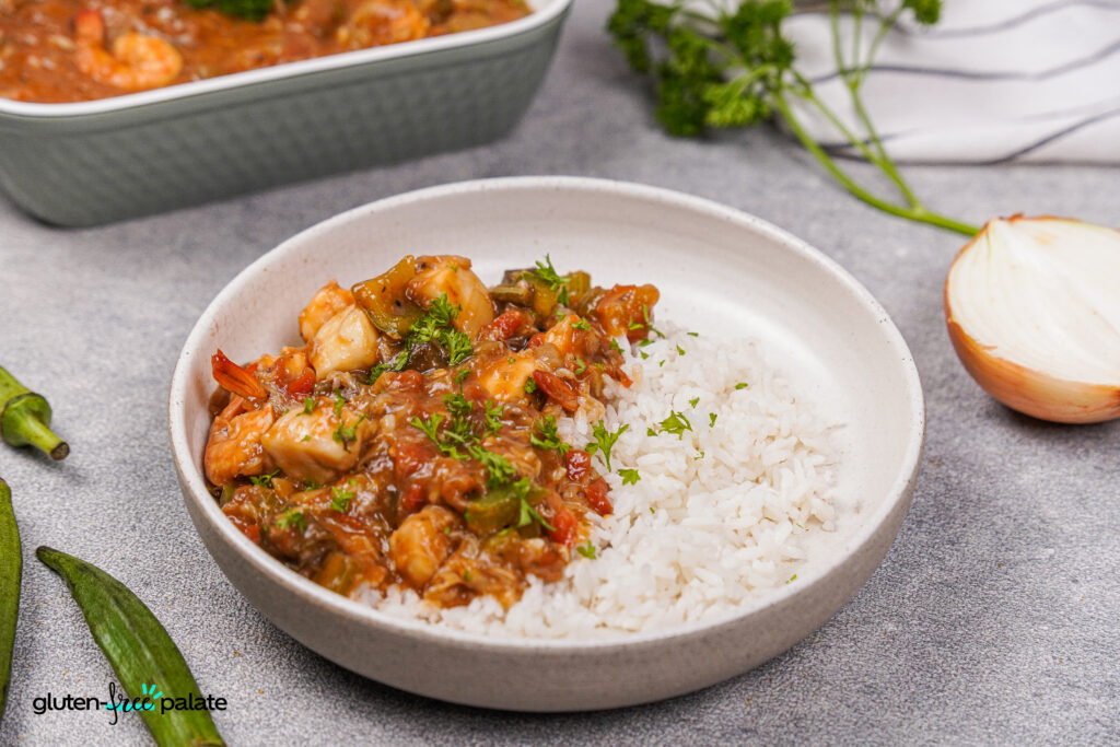 A bowl of seafood gumbo with rice and garnish.