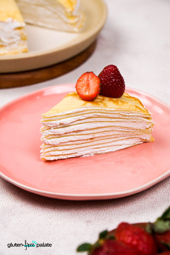 A slice of crepe cake on a pink plate with strawberries on top. Photo by Gluten-Free Palate.