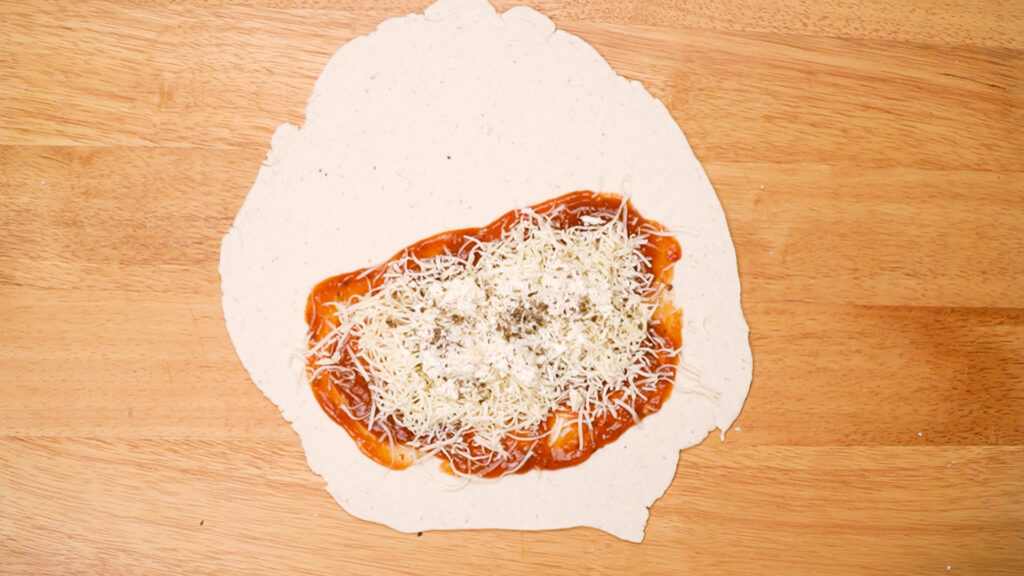Rolled-out gluten-free dough topped with marinara sauce, shredded cheese, ricotta, and Italian seasoning, ready to be folded. Photo by Gluten-Free Palate.