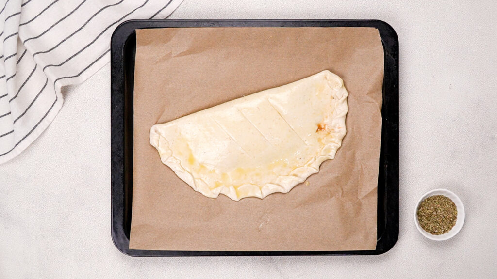 A shaped and sealed gluten-free calzone on parchment paper, brushed with egg wash, and vented with three slits, ready for baking. Photo by Gluten-Free Palate.