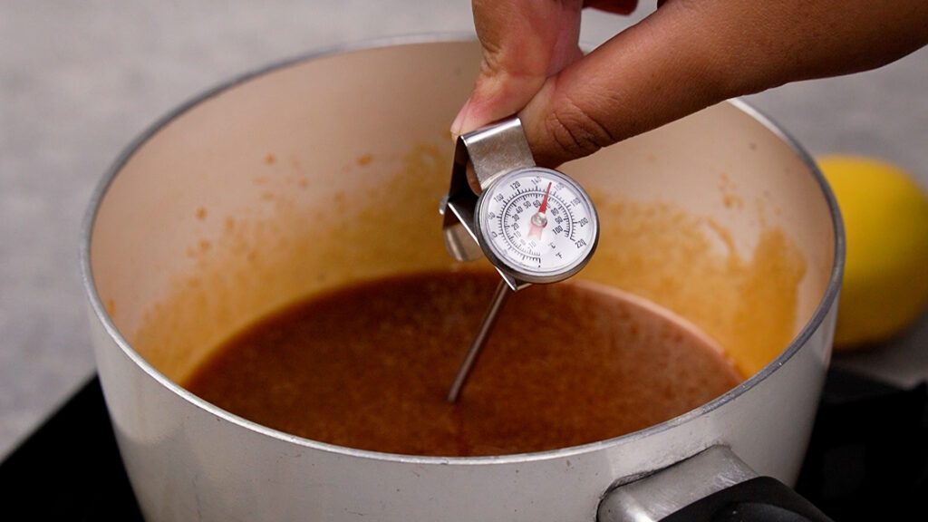Using a candy thermometer in a pot to check the syrup temperature.