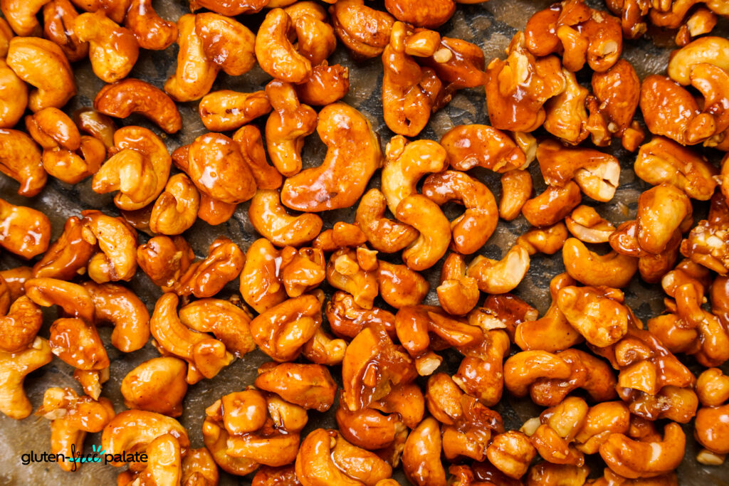 A close-up view of golden honey-roasted cashews spread on a baking sheet.