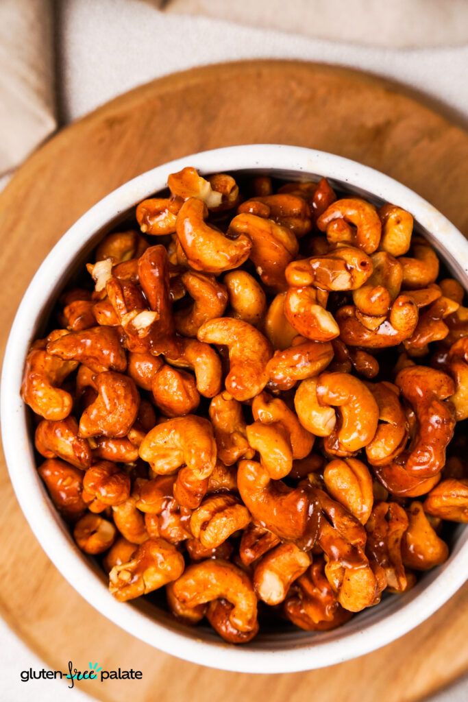 A bowl of honey roasted cashews. A close-up view of caramelized honey-roasted cashews in a white ceramic bowl.