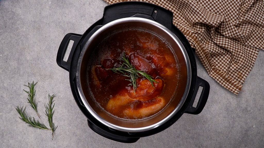 Step 4 Chicken breasts in an Instant Pot, covered in BBQ sauce and topped with sprigs of fresh rosemary.