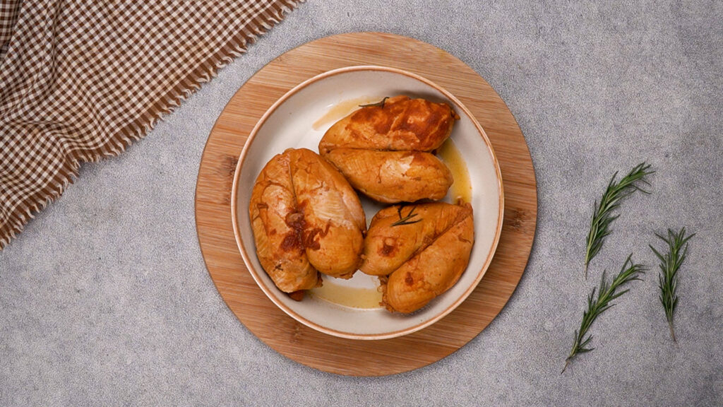 Step 7 Cooked chicken breasts coated in rich BBQ sauce, resting on a plate and ready to be shredded.