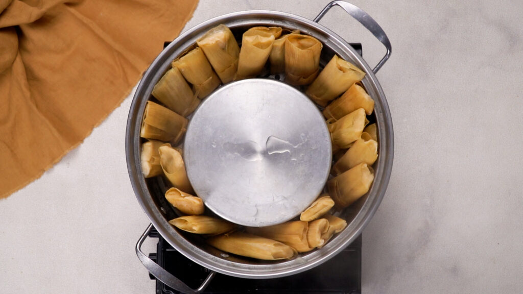 A steamer pot filled with upright tamales packed tightly and covered with a lid for steaming.