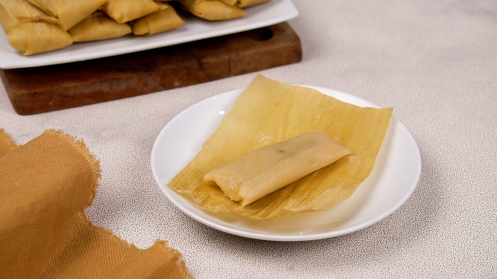 A freshly steamed gluten-free tamale placed on a corn husk on a white plate.