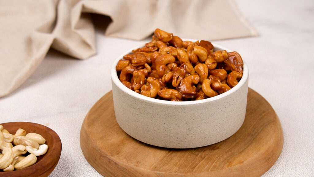 A Perfect Snack or Gift A bowl filled with freshly roasted honey-glazed cashews, placed on a wooden board.