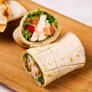 A fresh chicken wrap with lettuce, tomato, and dressing sliced in half.