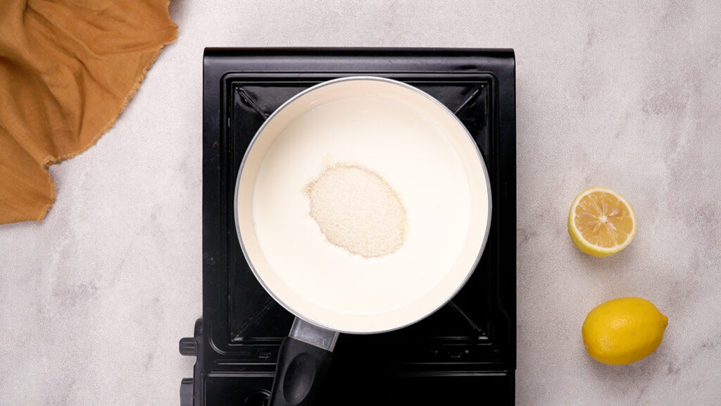 A saucepan filled with heavy cream and granulated sugar on a stovetop, ready to be heated.