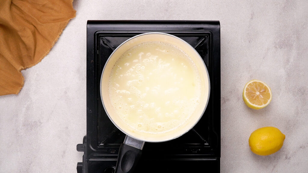 The cream and sugar mixture begins to simmer and bubble gently in the saucepan over medium heat.