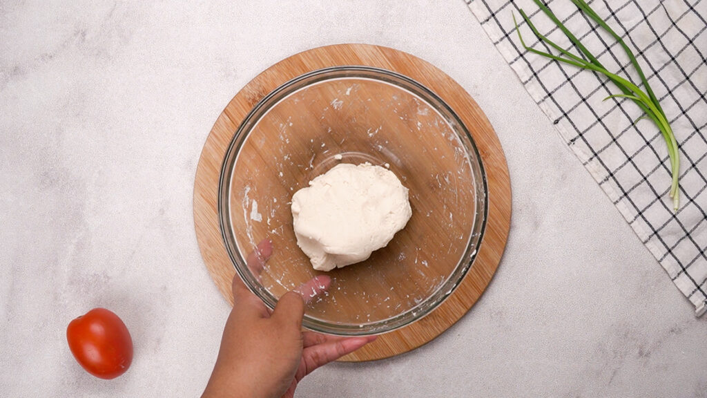 A ball of smooth gluten-free dough rests in a glass bowl on a wooden board, ready to be rolled out into wraps.