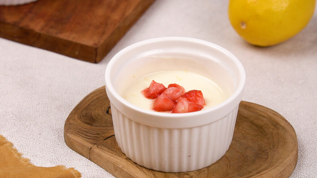 A finished lemon posset in a ramekin is garnished with chopped strawberries.