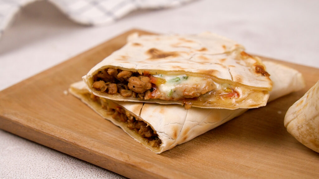 A cheesy gluten-free quesadilla with a crispy exterior and a savory filling is cut into triangles and stacked on a wooden serving board.